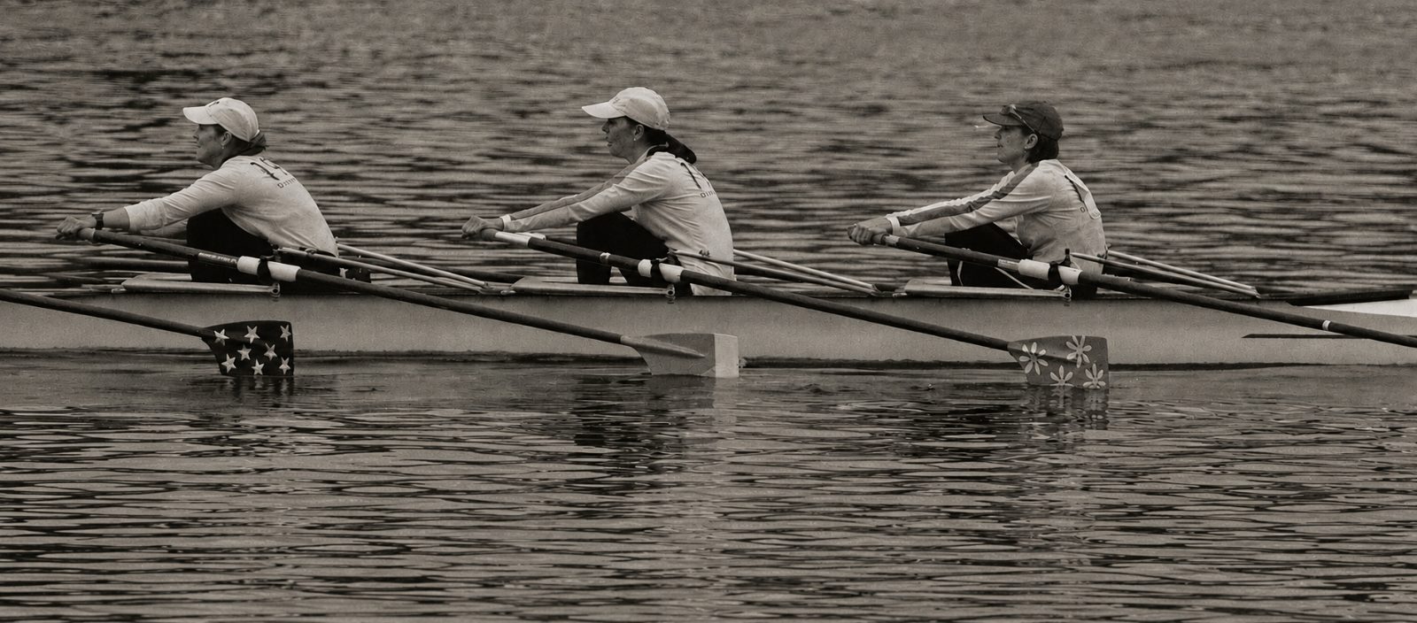 Three rowers in a coxless boat, mid-stroke on flat water